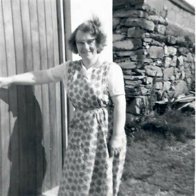 Hazel Tindall's mum wears a printed dress and glasses as she stands in front of a croft