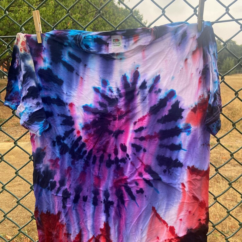 Pegged tie dye shirt hanging on a line outside, fence in the background