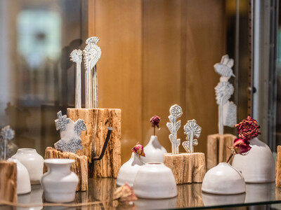 a glass cabinmate showing small ceramic pots and clay sculptures of flowers combined with pale wooden bases