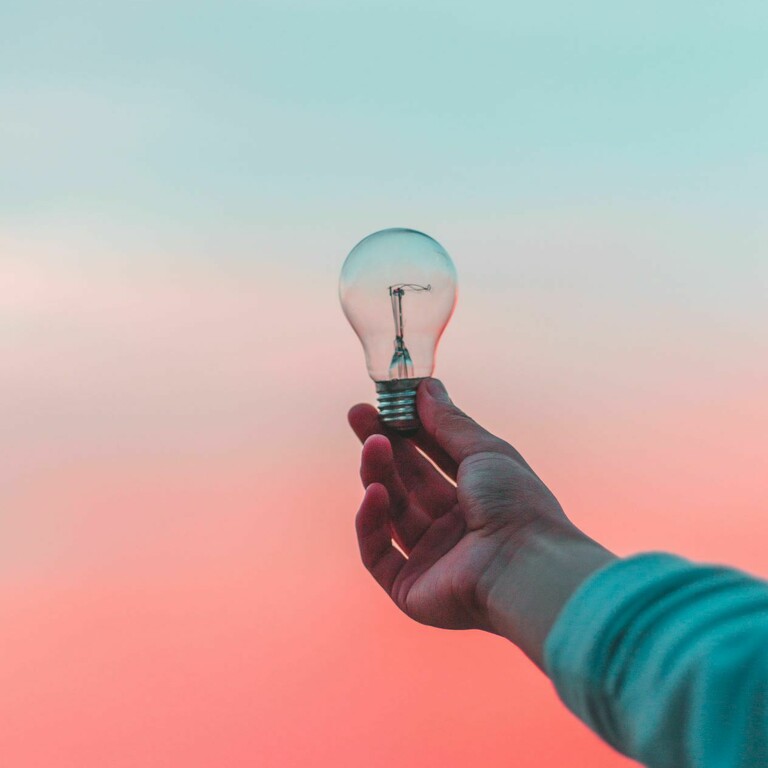 A hand holding up a light bulb during a sunset