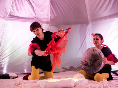 Two woman hold up puppets in a small tent