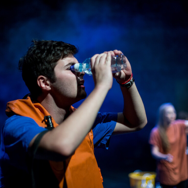 A man on stage uses a water bottle as a telescope.