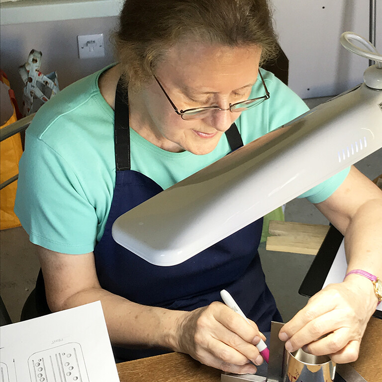 Christine Johnson in her studio measuring a metal container.
