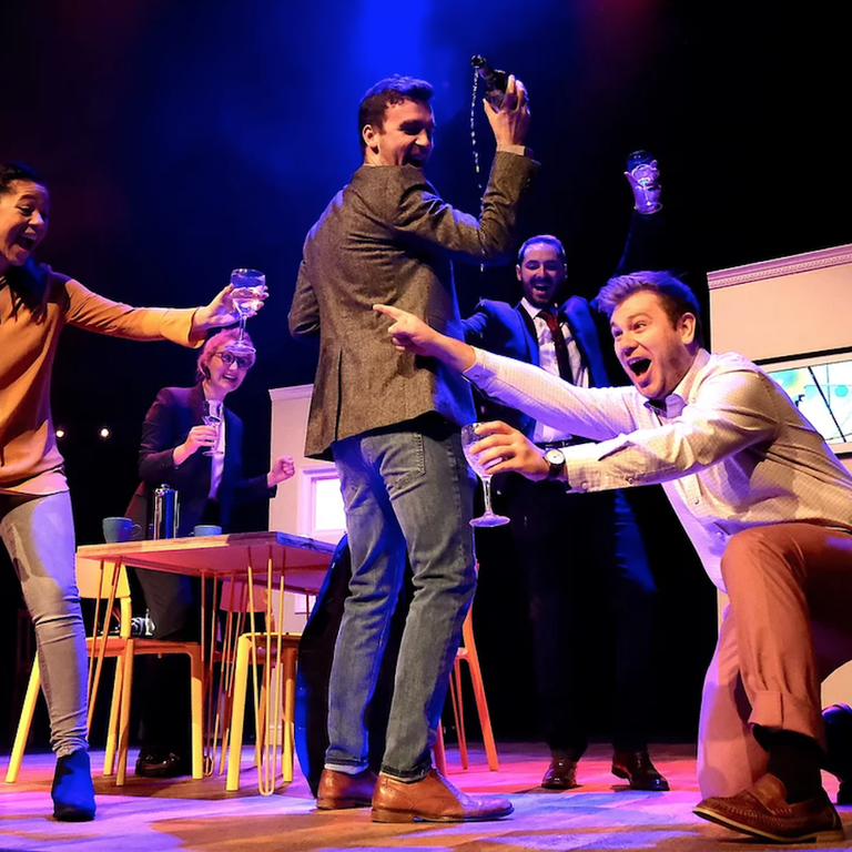 Stage scene of five young people at a dinner party with glasses of wine.
