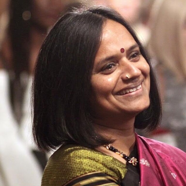A woman with mid-length dark hair smiling, wearing a bindi and sari.