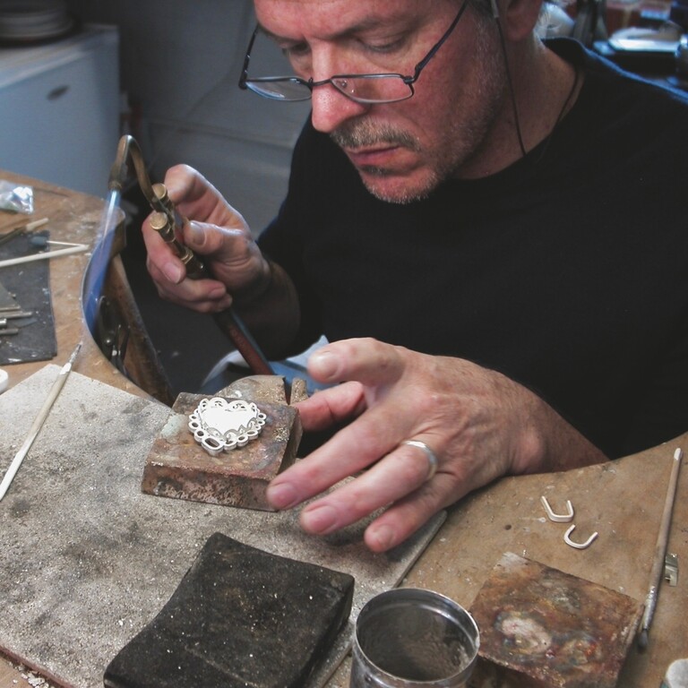 A man in a studio with a blow torch and a small heart shaped white decoration.