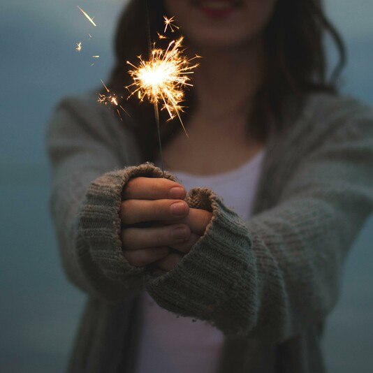 Woman with long brown hair wearing a cardigan, clutching a sparkler between her hands