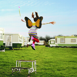 A young girl wearing butterfly wings jumping of a pedestal in a caravan park