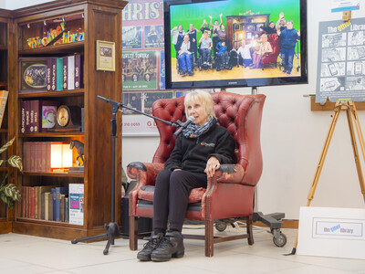 Performer sat in a red leather armchair with a microphone on a stand.