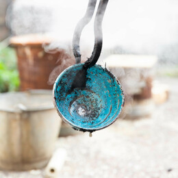 bright turquoise pot being held in iron tongs steaming after being dipped in bucket of water outside
