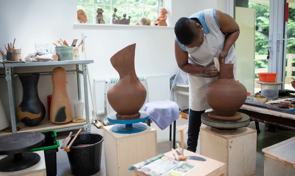 A woman works on smoothing out a pottery vase in her pottery studio