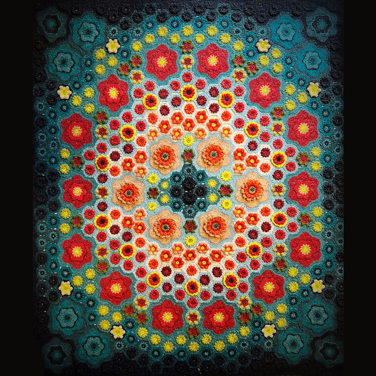 a crocheted blanket of flowers that begins red in the centre that transitions out to yellow, deep teal and black at the edges