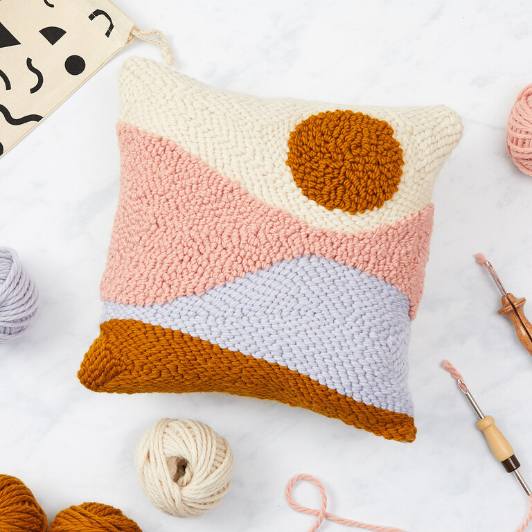 a needle punched pillow surrounded by balls of yarn and needlepunch tools