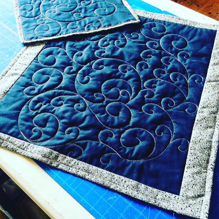 blue square of fabric with machine stiched quilting swirl patterns all over