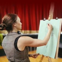 a photo of a lady standing in front of an artist's easel, sketching the form of a human body from a life model