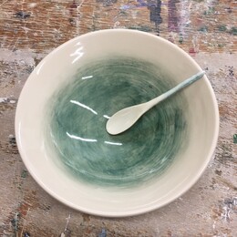 A hand made ceramic white and green bowl with a small ceramic spoon