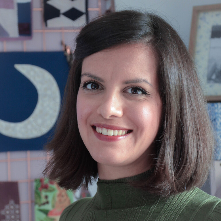 A woman named Yasmeen smiles and is wearing a green striped pullover.