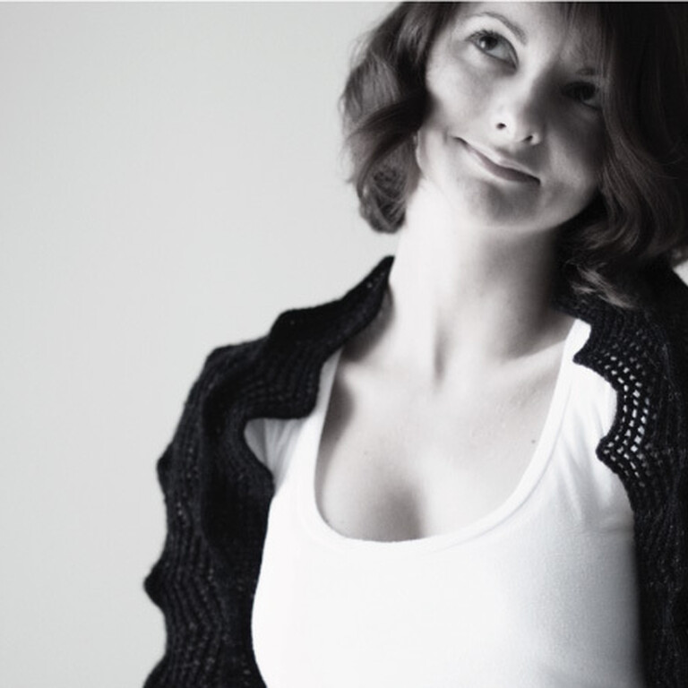 A woman named Olga smiles with a black knitted and tussled top and white t-shirt.