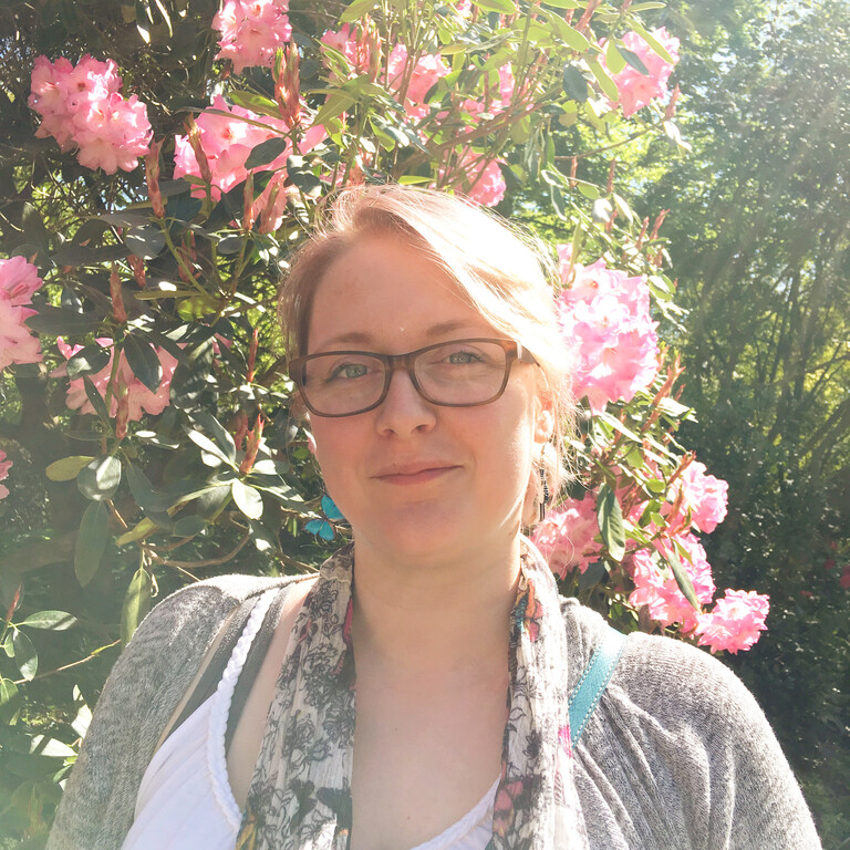 a lady with bloned hair and glasses stood by a rose bush