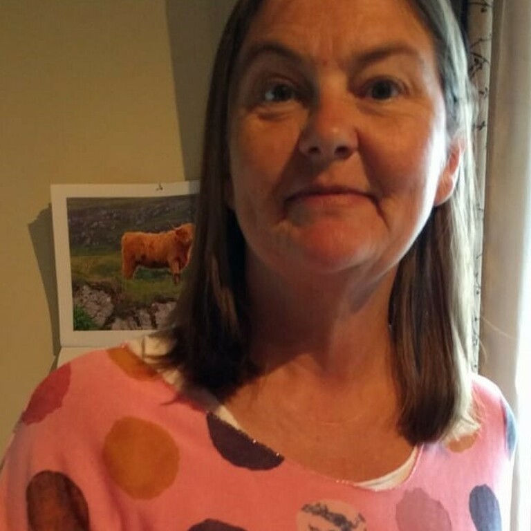 Photo of Julie Booker smiling in a dimly lit room wearing a pink polka dot top.