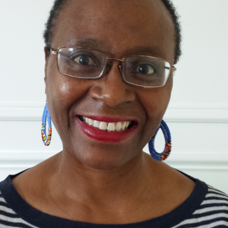 A black woman wearing glasses, a stripy top and multicoloured earrings, smiling.