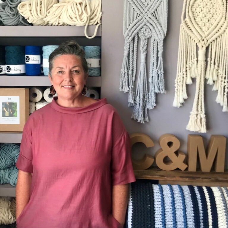 Photograph of a woman smiling in front of a yarn display