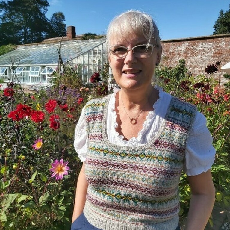 A woman called Amanda smiling outside in her garden thats full of flowers.