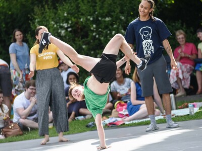 A dancer performs a break dance move on an outside stage.