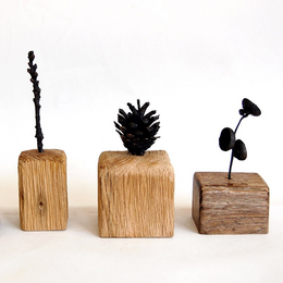 Three wooden block sculptures with foraged plants and sticks coming out the top