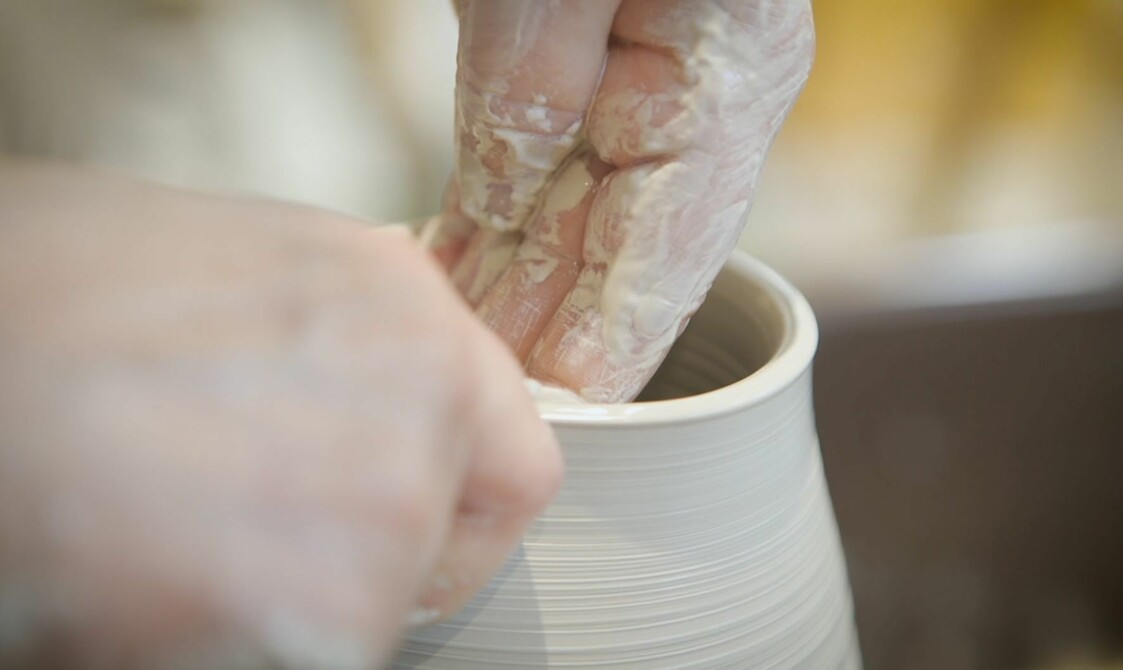 A clay covered hand shapes the inside of pottery