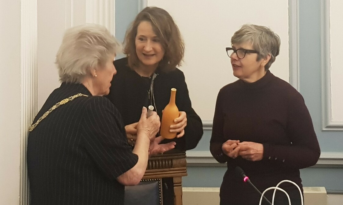 Three woman holding pottery talking to eachother.