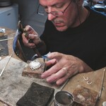 A man in a studio with a blow torch and a small heart shaped white decoration.