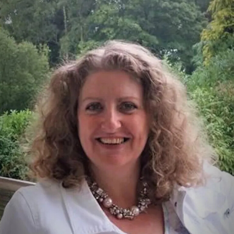 Carol Scicluna sat outside in a white blouse and chunky pearl necklace smiling.