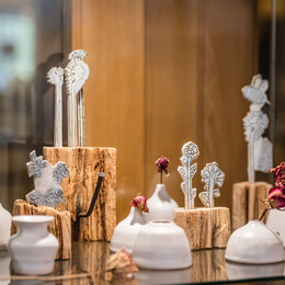 a glass cabinmate showing small ceramic pots and clay sculptures of flowers combined with pale wooden bases