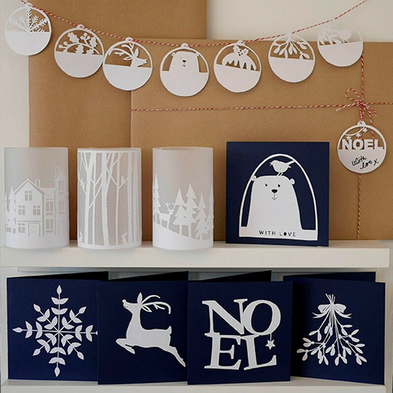 A photo of paper lanterns, a garland made out of papercut designs and papercut Christmas cards