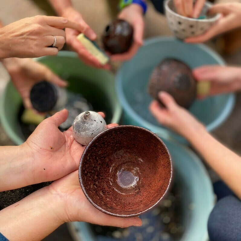 A photo of a group of people dipping ceramic bowls into water after a Raku session