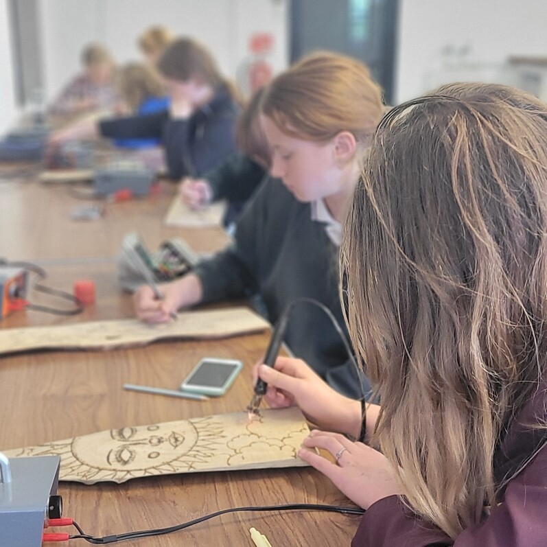 a photo of teenagers burning designs onto pieces of natural wood using a pyrography machine