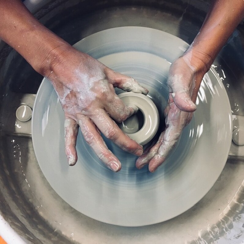 Two hands throwing clay onto a pottery wheel.