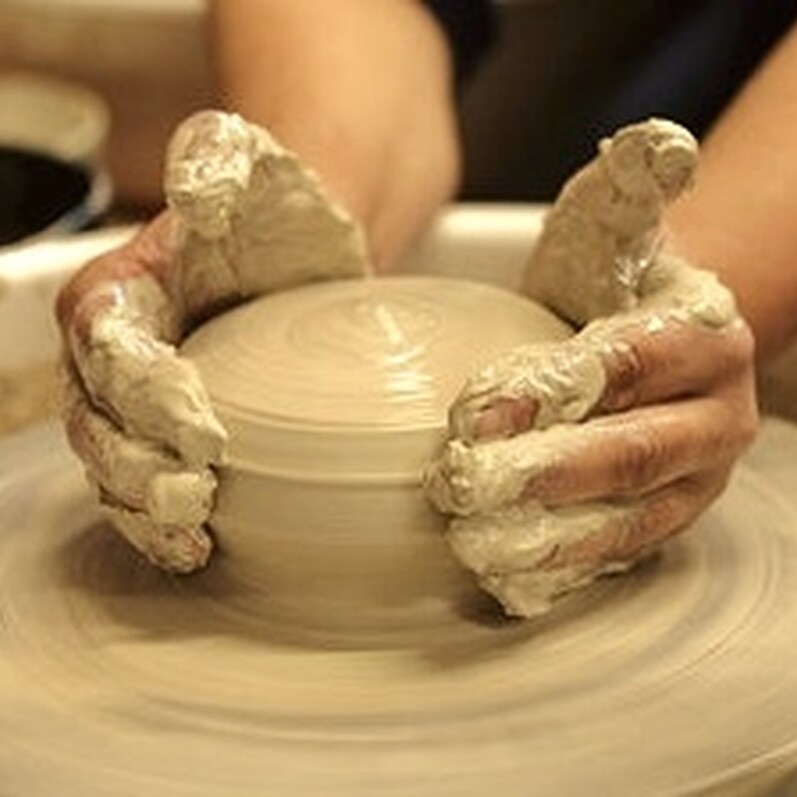 Two hands forming clay on a pottery wheel in a workshop