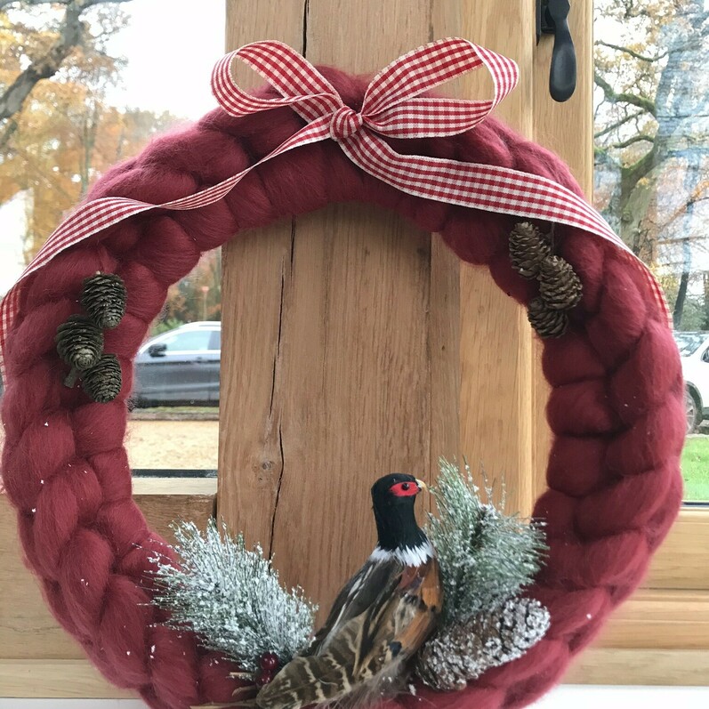A chunky knitted wreath decorated with pine cones, a bird and ribbon, sat on a window ledge.
