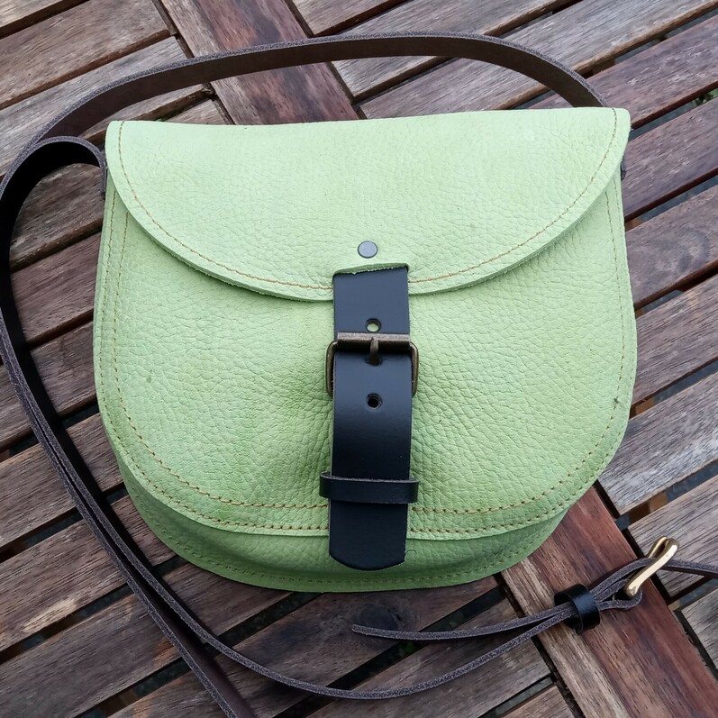 A green, brown and black leather shoulder bag laying on wooden boards.