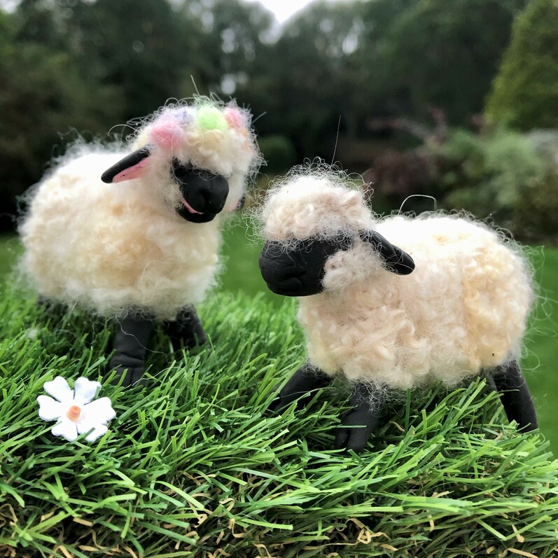Two needle felted sheep nestled amongst the grass and a small flower
