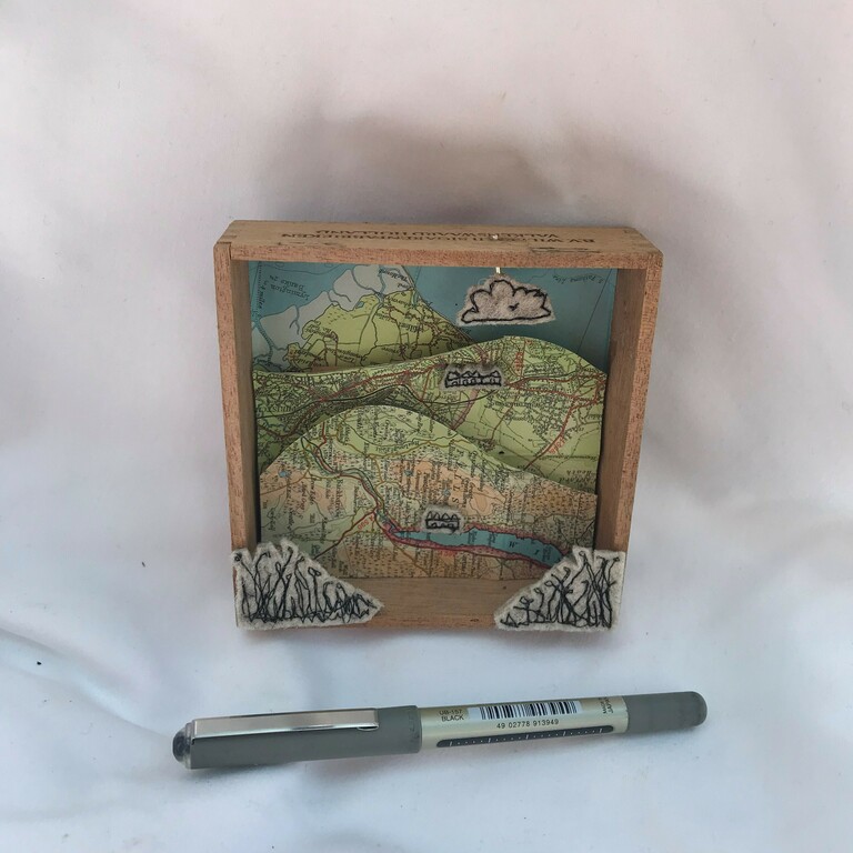 A small box with a layered map artwork inside and a pen beside it.