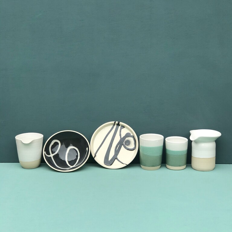 A blue background with a line of assorted pottery bowls, plates and jugs