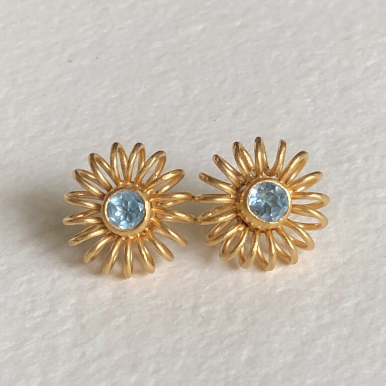 A pair of gold starburst earrings with pale blue stones in the centre