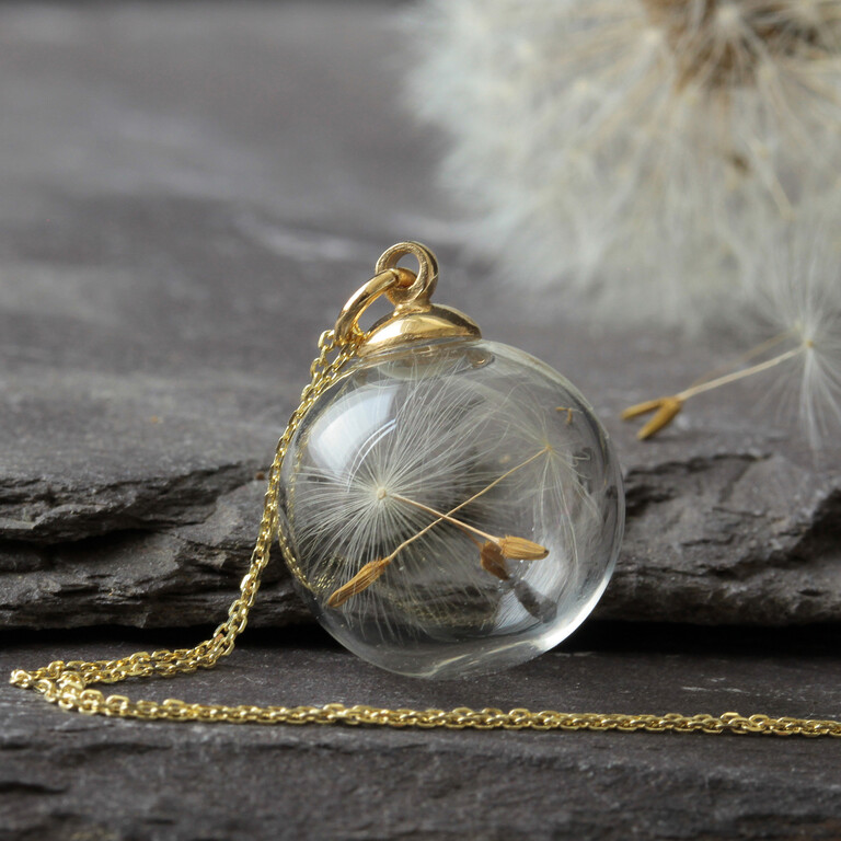A dandelion side is captured inside a glass sphere on a gold chain