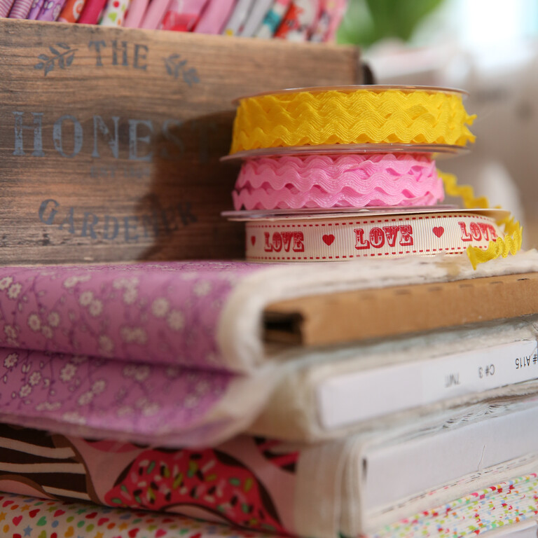 A pile of patterned fabrics with ribbons on top and a wooden container with more floral fabrics.