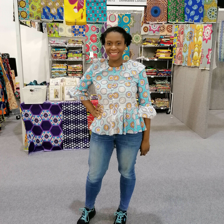 lady stood in front of her fabric selling stand with lots of bight printed African designs