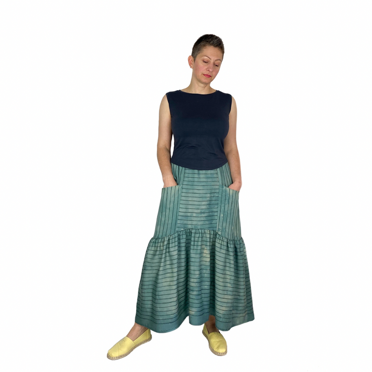 A woman wearing a black top, a long blue skirt and yellow shoes stands in front of a white background