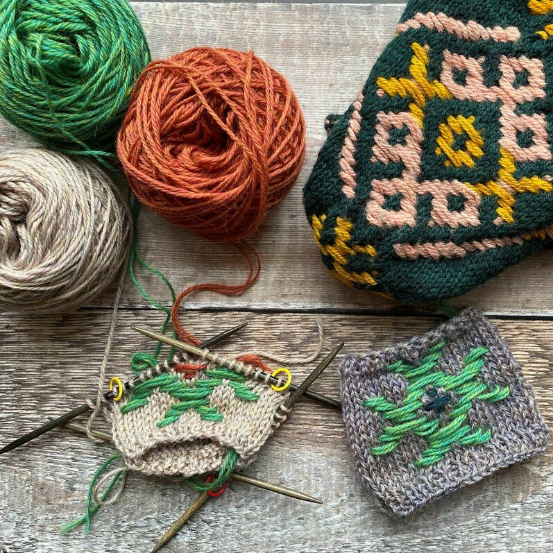 A wooden table with balls of yarn, knitted squares and knitting neeldes.